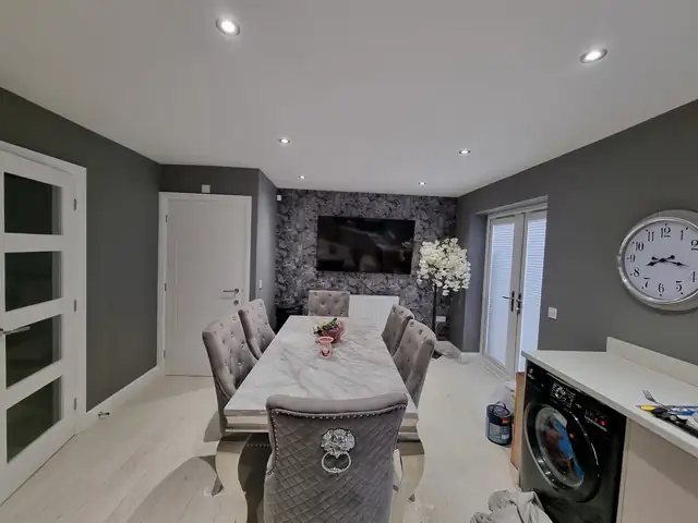 Dining room with grey walls and a dark floral feature wallpaper behind the TV